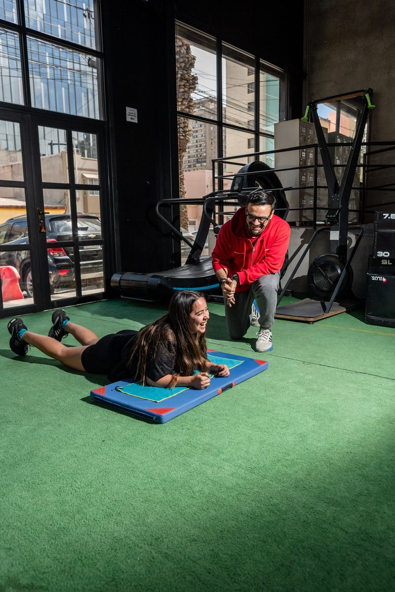 Un entrenador de Fit4Life, arrodillado, acompaña a una alumna que hace una plancha
