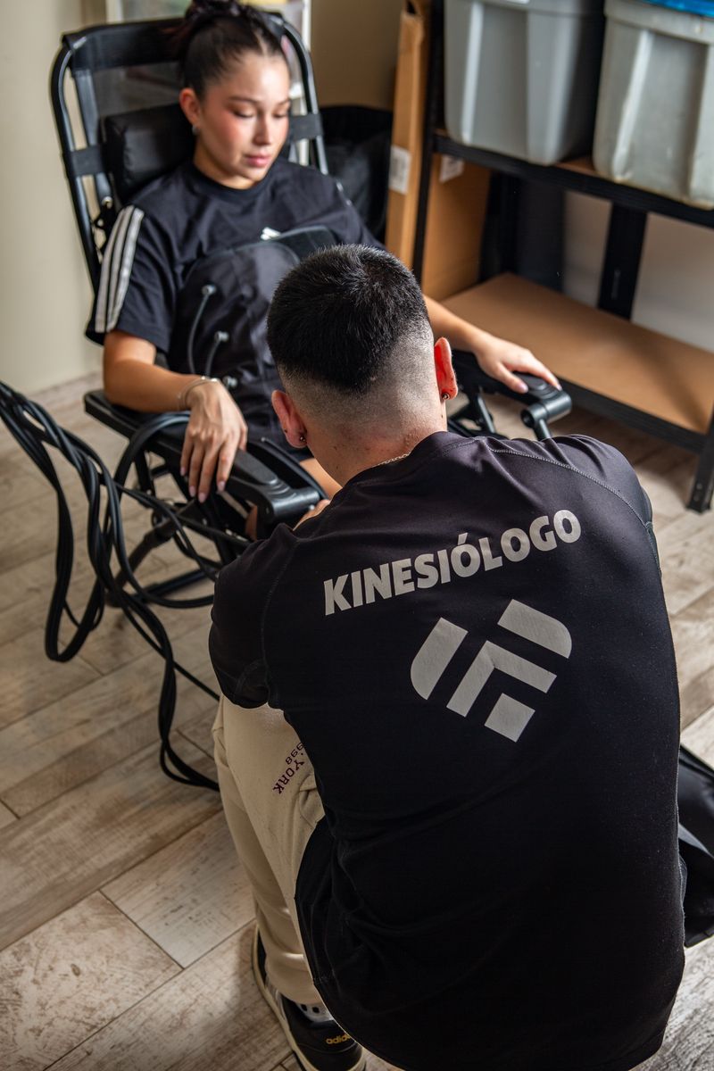 Un kinesiólogo de Fit4Life, de espaldas y con «Kinesiólogo» en la polera, atiende a una alumna