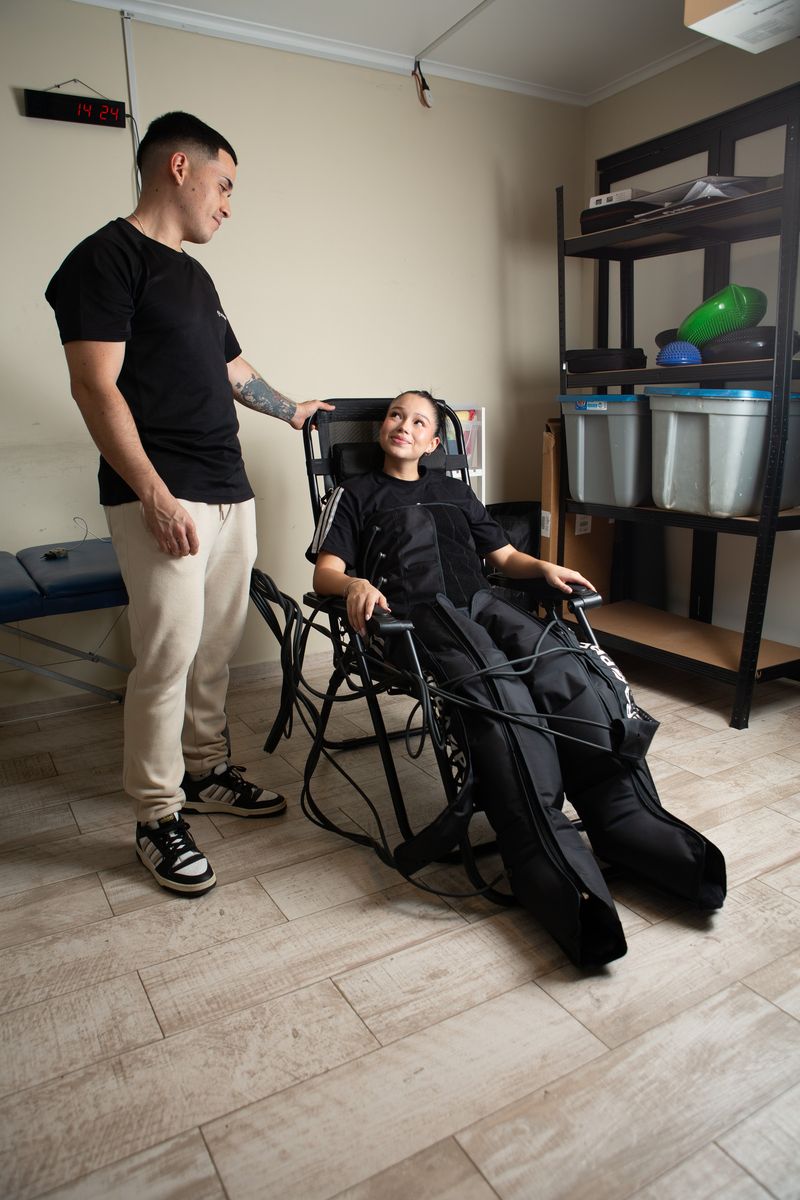 Una alumna con las botas de presoterapia en el sillón y el kinesiólogo a su lado