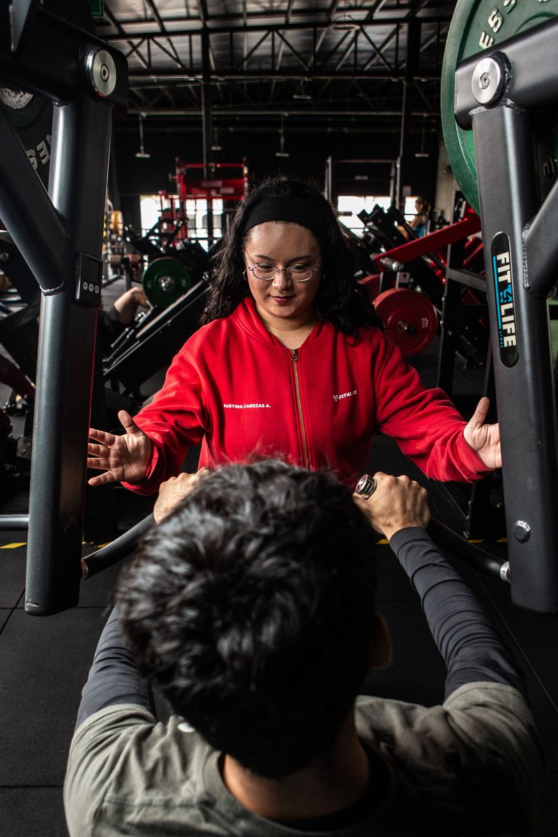 Una profesional de Fit4Life, de polerón rojo, le explica un ejercicio a un alumno