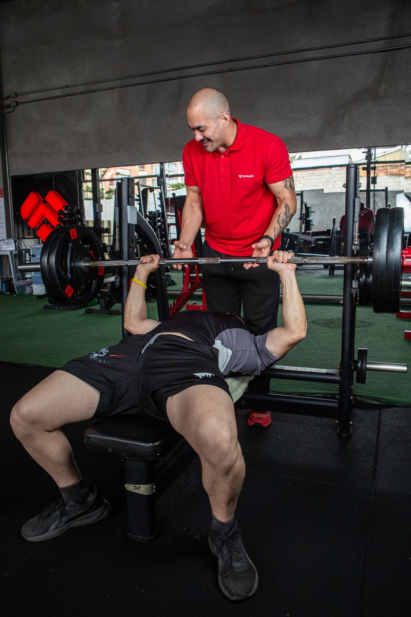 Un entrenador de Fit4Life asiste a un alumno en el press de banca